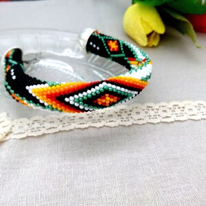 May include: A beaded bracelet with a geometric pattern in black, white, green, orange, and yellow.