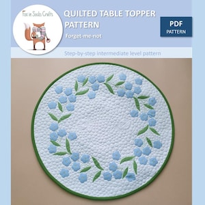 Könnte beinhalten: Ein PDF-Muster für einen gesteppten Tischläufer mit einem Vergissmeinnicht-Blumendesign. Das Muster ist für einen Quilter der mittleren Stufe geeignet.