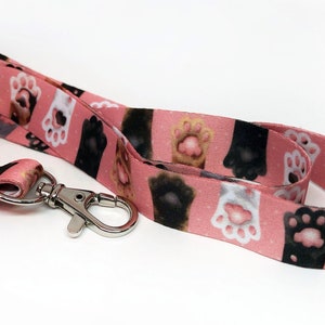 May include: A pink lanyard with a repeating pattern of colorful cat paw prints. The lanyard has a silver metal clip.