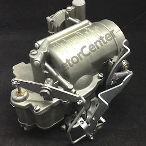 May include: A silver-coloured carburetor with multiple levers and a spring. The carburetor has a label that reads "Holley 1904 1BBL".