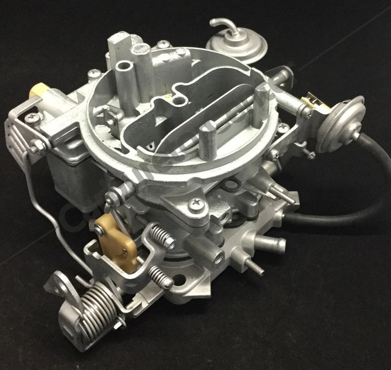 May include: A silver-colored carburetor with various mechanical components, including springs, tubes, and a fuel bowl. The automotive part is designed for internal combustion engines and is set against a black background.
