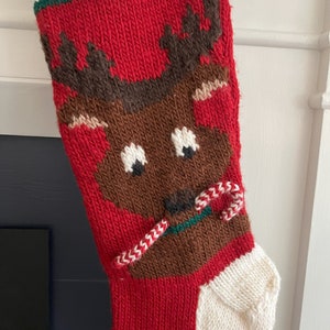 May include: A red knitted Christmas stocking with a brown reindeer face and candy cane. The stocking has a white cuff and green trim.