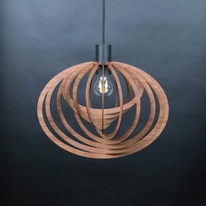 Puede incluir: Una l&aacute;mpara colgante de madera con un dise&ntilde;o circular y en capas. La l&aacute;mpara est&aacute; hecha de m&uacute;ltiples anillos conc&eacute;ntricos de madera, creando un patr&oacute;n geom&eacute;trico. Una sola bombilla es visible en el centro de la l&aacute;mpara.