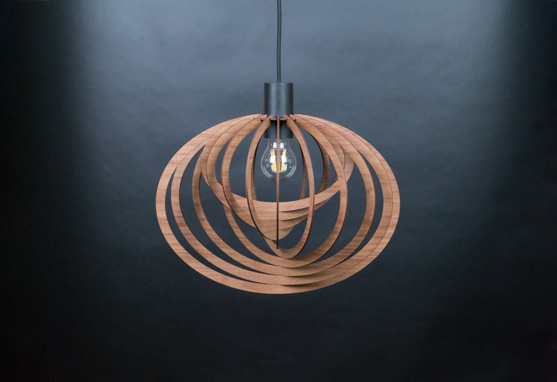 Puede incluir: Una l&aacute;mpara colgante de madera con un dise&ntilde;o circular y en capas. La l&aacute;mpara est&aacute; hecha de m&uacute;ltiples anillos conc&eacute;ntricos de madera, creando un patr&oacute;n geom&eacute;trico. Una sola bombilla es visible en el centro de la l&aacute;mpara.