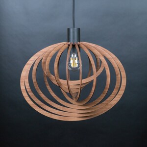 Puede incluir: Una l&aacute;mpara colgante de madera moderna con un dise&ntilde;o circular. La l&aacute;mpara est&aacute; hecha de m&uacute;ltiples capas de madera que se apilan y curvan para crear una forma esf&eacute;rica. La l&aacute;mpara tiene un cable negro y una base de metal negro.