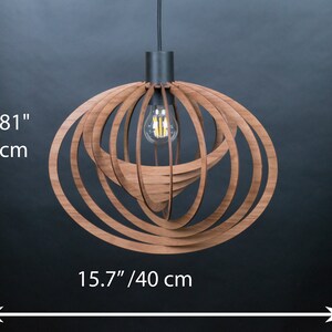 Puede incluir: Una l&aacute;mpara colgante de madera con un dise&ntilde;o circular. La l&aacute;mpara tiene 30 cm de alto y 40 cm de ancho. Tiene un acabado de madera marr&oacute;n y un cable de metal negro.