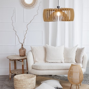 May include: A white couch with white pillows sits in a living room with a woven rug, a woven side table, a woven lamp, and a woven storage basket. The room is decorated in a bohemian style.