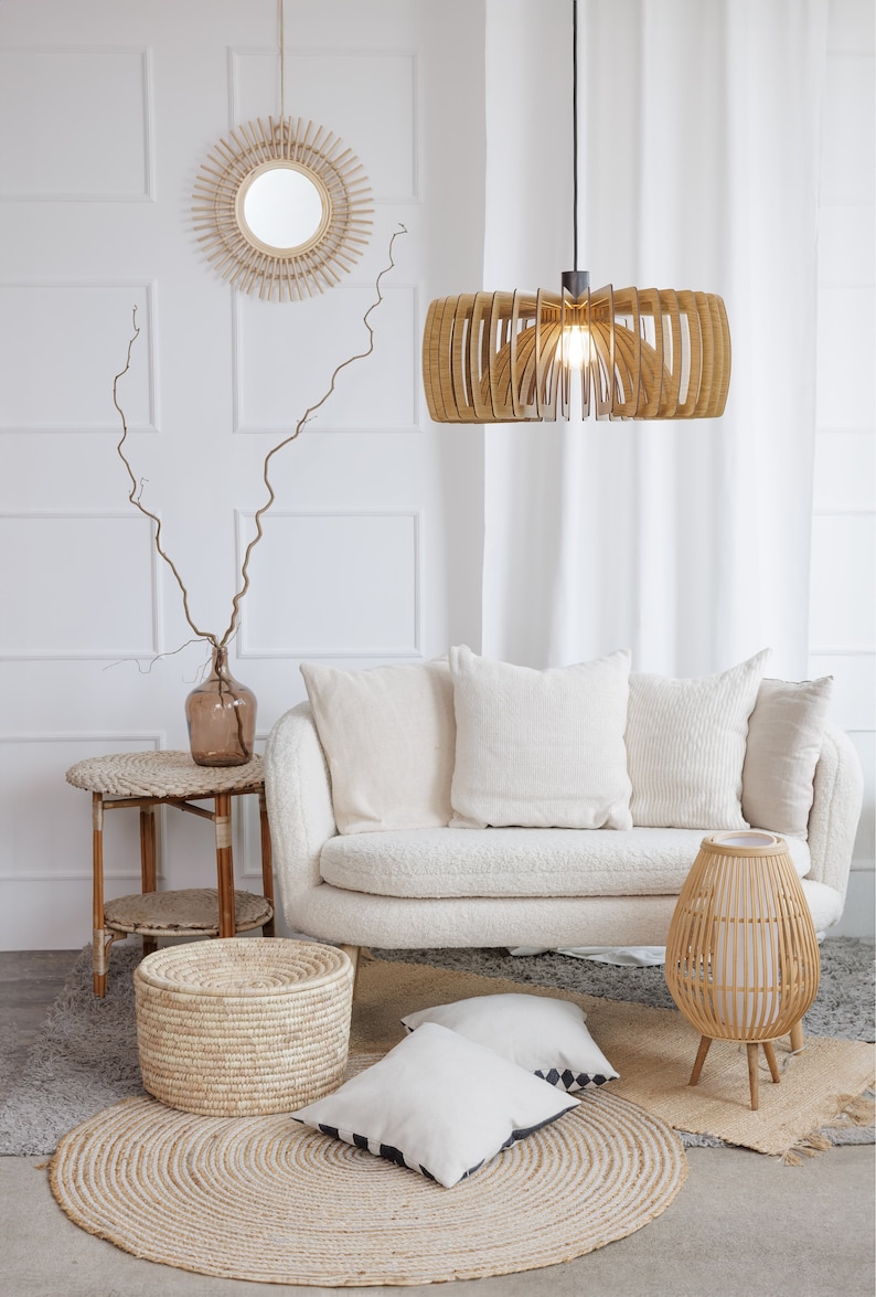 May include: A white couch with white pillows sits in a living room with a woven rug, a woven side table, a woven lamp, and a woven storage basket. The room is decorated in a bohemian style.
