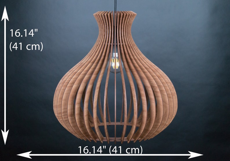 May include: A wooden pendant light fixture with a bulb, 16.14 inches (41 cm) in height and width. The light has a unique, open design with vertical wooden slats, creating a warm, ambient glow. The fixture is suspended from a black cord.