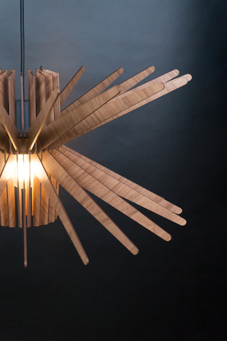K&ouml;nnte beinhalten: Eine Holz-Pendelleuchte mit einem Sternburst-Design. Die Leuchte besteht aus d&uuml;nnen Holzlamellen, die von einem zentralen Punkt nach au&szlig;en strahlen. Die Leuchte wird von einer einzigen Gl&uuml;hbirne beleuchtet.