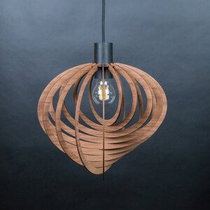 Puede incluir: Una l&aacute;mpara colgante de madera con un dise&ntilde;o geom&eacute;trico. La luz est&aacute; hecha de finas tiras de madera que est&aacute;n dispuestas en un patr&oacute;n circular. La luz cuelga de un cable negro y tiene una sola bombilla.