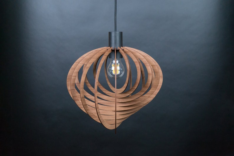 Puede incluir: Una l&aacute;mpara colgante de madera con un dise&ntilde;o geom&eacute;trico. La luz est&aacute; hecha de finas tiras de madera que est&aacute;n dispuestas en un patr&oacute;n circular. La luz cuelga de un cable negro y tiene una sola bombilla.