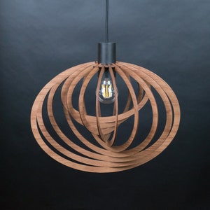 Puede incluir: Una l&aacute;mpara colgante de madera con un dise&ntilde;o circular y en espiral. La l&aacute;mpara est&aacute; hecha de m&uacute;ltiples tiras finas de madera que se entrelazan para crear un aspecto &uacute;nico y moderno. La l&aacute;mpara cuelga de un cable negro y tiene una base de metal negro.