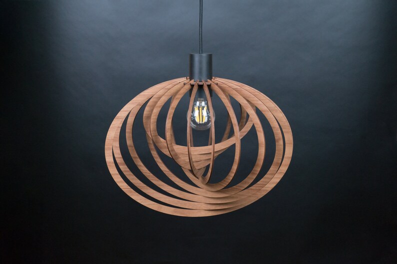 Puede incluir: Una l&aacute;mpara colgante de madera con un dise&ntilde;o circular y en espiral. La l&aacute;mpara est&aacute; hecha de m&uacute;ltiples tiras finas de madera que se entrelazan para crear un aspecto &uacute;nico y moderno. La l&aacute;mpara cuelga de un cable negro y tiene una base de metal negro.