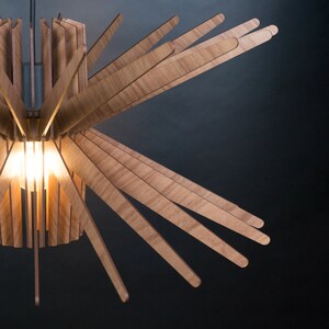 May include: A wooden pendant light fixture with a starburst design. The light fixture is made of thin, wooden slats that radiate outwards from a central point. The light fixture is illuminated by a single light bulb.