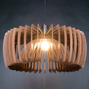 May include: A modern wooden pendant light fixture with a geometric design. The light is made of thin strips of wood that are arranged in a circular pattern. The light is turned on and illuminates the room with a warm glow.