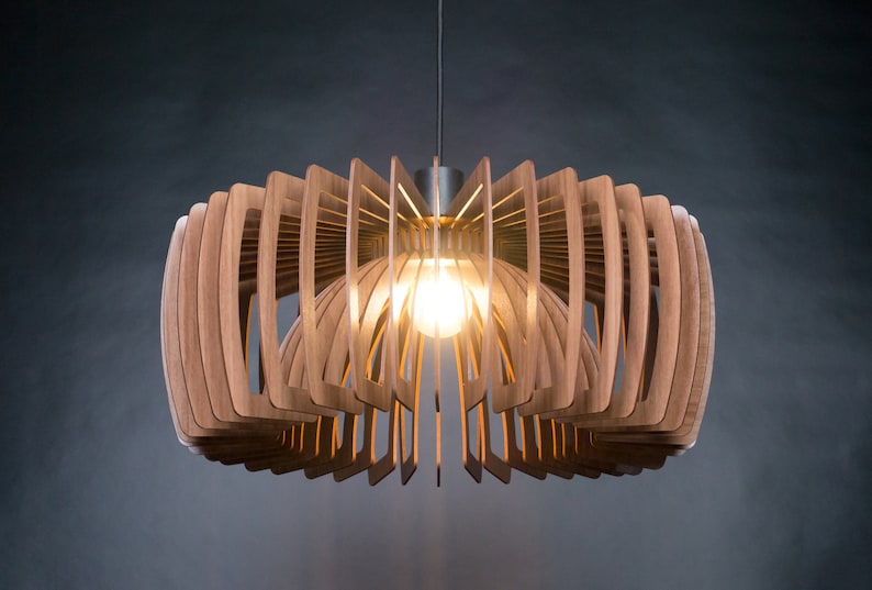 May include: A modern wooden pendant light fixture with a geometric design. The light is made of thin strips of wood that are arranged in a circular pattern. The light is turned on and illuminates the room with a warm glow.