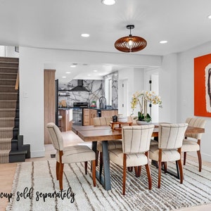 May include: A modern dining room with a wooden table and six chairs. The table has a dark wood finish and the chairs have a light beige fabric upholstery. There is a rug on the floor with a white and gray striped pattern. A large orange painting hangs on the wall. The room has a white ceiling with recessed lighting.