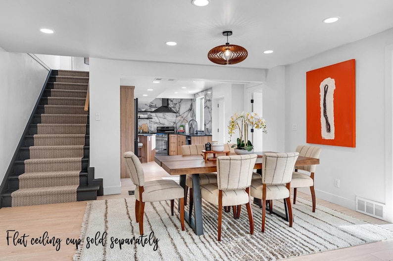 May include: A modern dining room with a wooden table and six chairs. The table has a dark wood finish and the chairs have a light beige fabric upholstery. There is a rug on the floor with a white and gray striped pattern. A large orange painting hangs on the wall. The room has a white ceiling with recessed lighting.