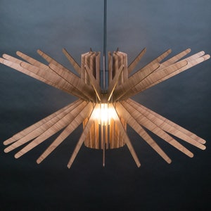 May include: A wooden ceiling light fixture with a starburst design. The light fixture is made of thin, light brown wooden slats that radiate outward from a central cylinder. The light fixture is illuminated by a single light bulb in the center.