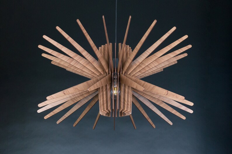 May include: A wooden ceiling light fixture with a starburst design. The light fixture is made of thin, wooden slats that radiate outwards from a central point. The light fixture is suspended from the ceiling by a thin wire.