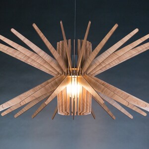 May include: A wooden pendant light fixture with a cylindrical shade and multiple wooden slats extending outward, creating a starburst effect. The light is on and illuminating the room.