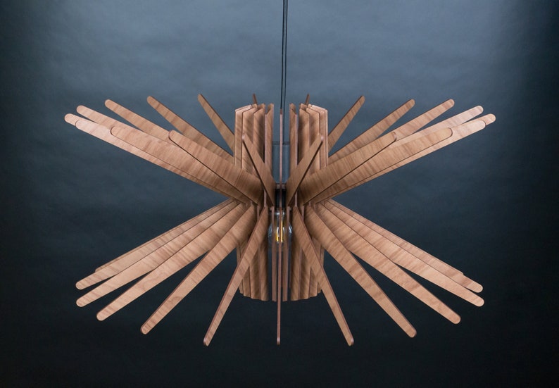 K&ouml;nnte beinhalten: Eine Deckenleuchte aus Holz mit einem Sternburst-Design. Die Leuchte besteht aus d&uuml;nnen Holzlamellen, die von einem zentralen Zylinder nach au&szlig;en strahlen. Die Leuchte wird mit einem einzigen Kabel an der Decke befestigt.
