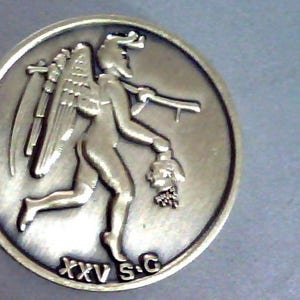 May include: A silver-toned metal coin with a raised image of a winged figure carrying a severed head. The figure is running to the right and the coin has the text "XXV S.G." inscribed on the bottom.