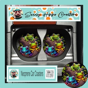 May include: Two round neoprene car coasters featuring a colorful illustration of three frogs perched on a tree branch. The design includes a green frog, a yellow-green frog, and a blue frog. The text Sassy Hippo Creations and Neoprene Car Coasters is visible.