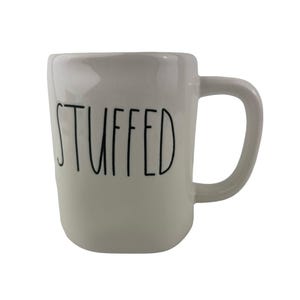 May include: A white ceramic mug with a glossy finish and a rounded handle. The word STUFFED is printed on the front in a tall, thin, black sans-serif font. The mug has a slightly irregular, hand-crafted appearance with a smooth, curved body shape.