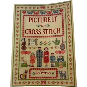 May include: A cross-stitch pattern with the text "PICTURE IT in CROSS STITCH" in a red frame. The design includes a family, musical instruments, hearts, butterflies, and the name "Jo Verso". The border is decorated with floral and star patterns.