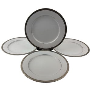 May include: Four white ceramic plates with silver rims. The plates have a simple, elegant design, with a wide white centre and a thin silver band around the edge. The rims have a textured pattern.