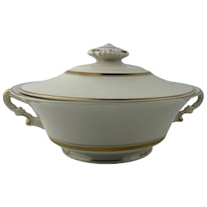 May include: Cream-colored covered serving dish with gold trim. The dish has a rounded shape with two handles and a lid with a decorative knob. The gold trim accents the edges of the dish and lid, creating an elegant look.