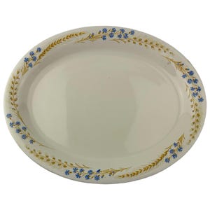 May include: An oval-shaped white ceramic serving platter featuring a decorative border pattern of golden wheat stalks and small blue cornflower blossoms arranged along the rim of the dish, leaving the center of the platter plain and smooth.