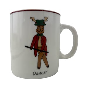 May include: White ceramic mug featuring a cartoon reindeer dressed as a dancer. The reindeer wears a green hat, red jacket, and holds a cane. The word "Dancer" is printed at the bottom of the mug.