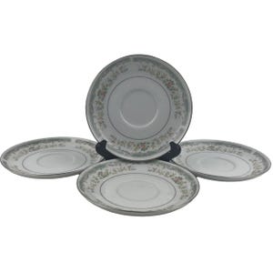 May include: Four white porcelain saucer plates with a floral design border in shades of green, pink, and yellow. The saucers have a silver trim and are arranged on a black stand.
