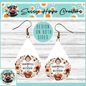 May include: Teardrop-shaped earrings featuring a white background with a Thanksgiving-themed graphic. The design includes a turkey, a basket of produce, and autumn flowers arranged in a wreath with the text Thankful & Blessed.