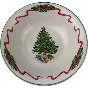 May include: A white ceramic Christmas bowl with a green rim and a festive design. The bowl features a decorated Christmas tree with Santa on top, surrounded by gifts. Red ribbons and holly accents adorn the rim.