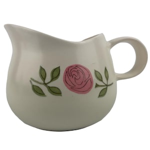 Può includere: Brocca in ceramica color crema con corpo arrotondato e manico. La brocca è decorata con una rosa rosa e foglie verdi. La brocca ha un beccuccio per versare facilmente.