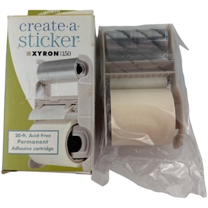 May include: A Xyron 150 create-a-sticker machine with a 20-ft. acid-free permanent adhesive cartridge. The set includes a cardboard box with green and white branding and a plastic-wrapped adhesive applicator unit with rollers.