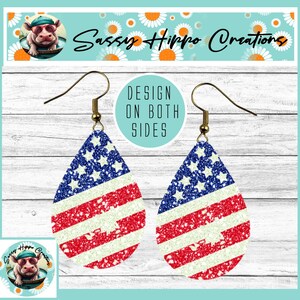 May include: A pair of teardrop-shaped earrings featuring a glittery American flag pattern with red, white, and blue stripes and stars. The earrings have gold-toned metal fishhook wires and a circular text graphic stating DESIGN ON BOTH SIDES.