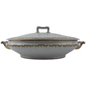 Może przedstawiać: Biała porcelanowa salaterka z pokrywką i uchwytami. Naczynie posiada złote wykończenia i dekoracyjny kwiatowy wzór na obrzeżu. Pokrywka posiada uchwyt ułatwiający podnoszenie. Klasyczny element do serwowania potraw.