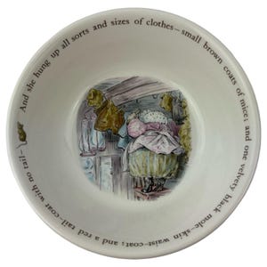 Puede incluir: Cuenco de cerámica blanco con una ilustración detallada de una escena con ropa y texto alrededor del borde. La ilustración presenta una cesta de ropa y el texto "And she hung up all sorts and sizes of clothes".