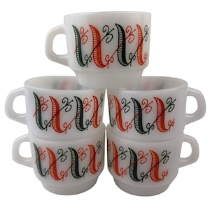 May include: A stack of six white ceramic coffee cups. Each cup features a handle and is decorated with a repeating pattern of red, black, and green vertical lines with decorative swirls. The cups are stacked in a pyramid shape.