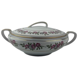 May include: A white porcelain serving dish with a lid, featuring a floral pattern in pink and gray. The dish has gold trim and handles on both sides. The lid has a loop handle.