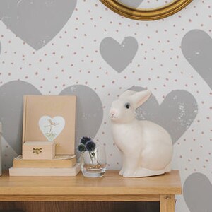 May include: A nursery room with a white wall covered in a gray heart pattern with pink dots. A wooden shelf with books and boxes is on the left side of the image. A white rabbit figurine is on the shelf. A gray pillow with a star shape is in a gold frame on the wall. The text "Buy on patternsColoray Etsy Shop" is on the right side of the image.