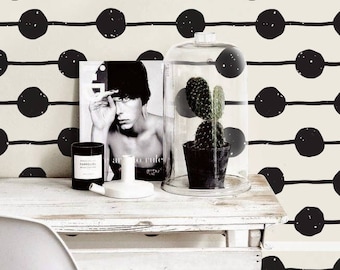 May include: Black and white geometric wallpaper with a repeating pattern of circles and lines. The wallpaper is shown in a room with a white desk, a white chair, and a glass cloche with a cactus plant.