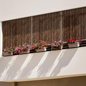 May include: A white building with a balcony featuring a row of potted pink and red flowers. The balcony has a wooden slatted window behind the flowers.