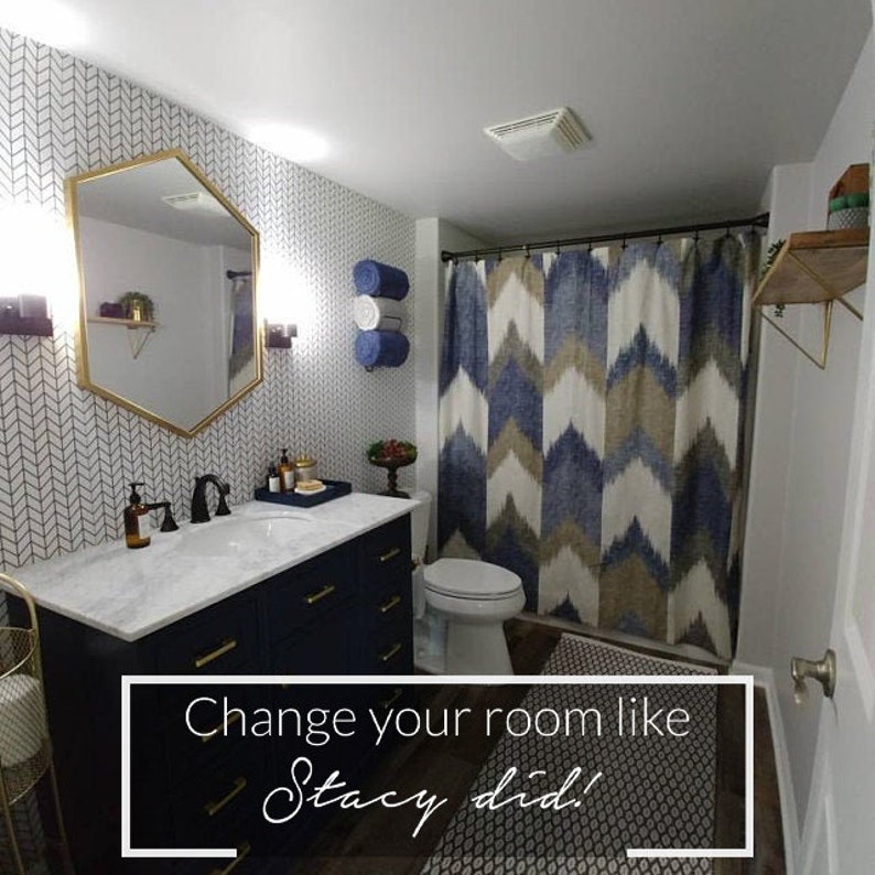 May include: A bathroom with a navy blue vanity, white marble countertop, and gold hardware. The bathroom has a white chevron patterned wallpaper, a white toilet, and a shower with a blue and brown geometric patterned shower curtain. The text "Change your room like Stacy did!" is on a black and white patterned rug.