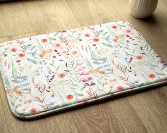 May include: A white bath mat with a floral pattern featuring pink, orange, and green watercolor flowers and leaves.